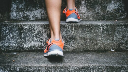 person wearing orange and gray Nike shoes walking on gray concrete stairs