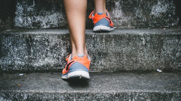 person wearing orange and gray Nike shoes walking on gray concrete stairs